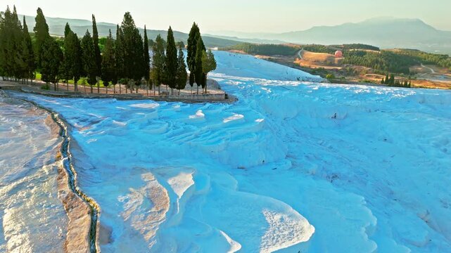 Drone view of Travertines of Pamukkale, Turkey. Thermal pools, white limestone terraces and green trees create a scenic natural landmark.