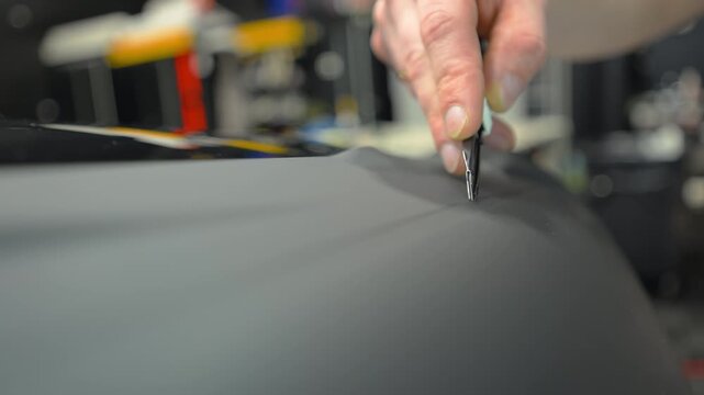 Close up of a cutting matte black vinyl wrap on a car body panel in a workshop. Automotive detailing process with protective film installation, smooth matte finish and precision work.