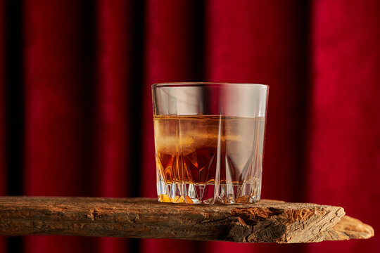 Glass of whisky bourbon on rustic wood with red curtain