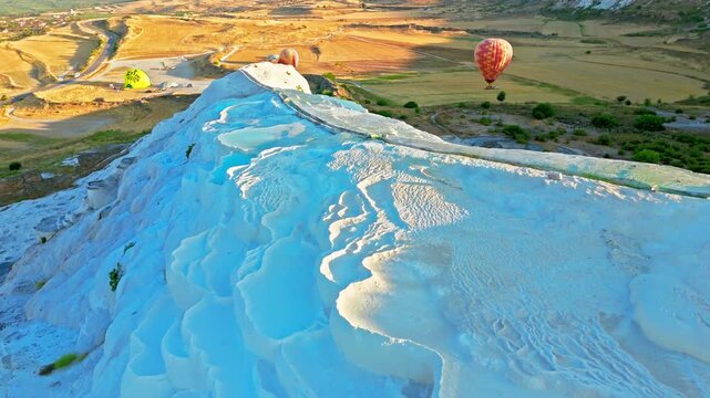 Aerial view of Travertines of Pamukkale, Turkey. Hot air balloon rises over turquoise pools and white limestone terraces at sunrise.