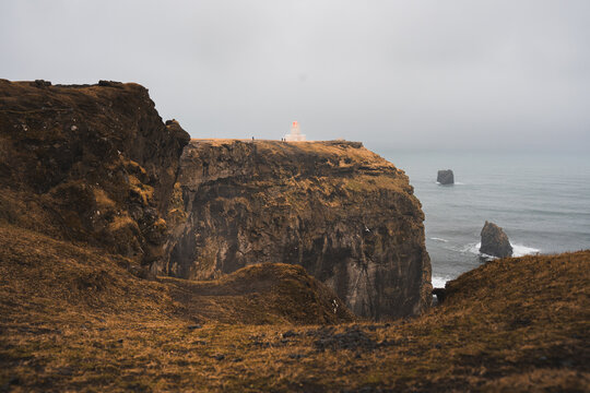 Rugged Iceland sea cliffs with lighthouse in misty weather