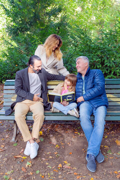 Three-generation family reading together on a park bench