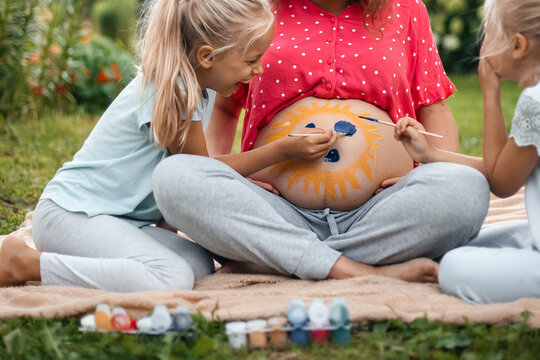 Happy family painting sun on pregnant belly outdoors