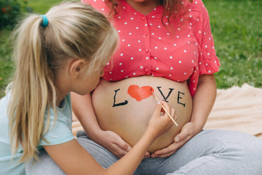 Happy family painting love on pregnant belly outdoors