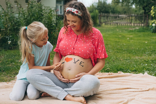 Pregnant mother and daughter painting love on baby bump