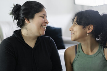 Fototapeta premium Smiling Latina mother and daughter look at each other and share a heartwarming moment together at home.