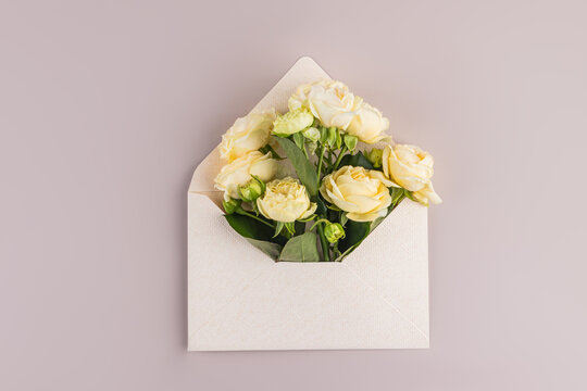 Cream rose bouquet in envelope on pastel background