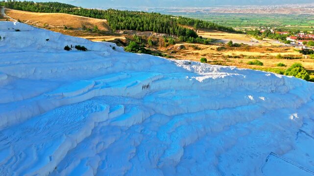 Drone view of Travertines of Pamukkale, Turkey. Blue pools, white limestone terraces and distant fields create a scenic travel view.