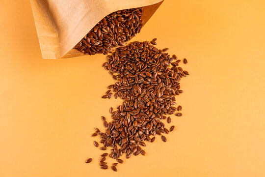 Flax seed spilling from paper bag on pastel background