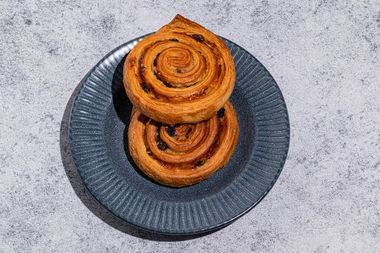 Two raisin swirl pastries on dark plate, top view