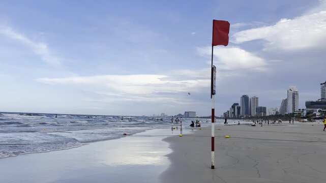 Video of a red warning flag on a beach by the sea, indicating dangerous swimming conditions and restricted access to water. Coastal safety concept with ocean waves and seaside atmosphere.