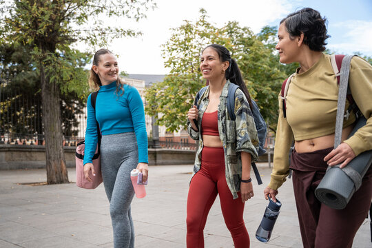 Multiethnic women walking outdoors with yoga mats and bags