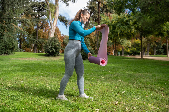 Woman unrolling yoga mat on grass in autumn park