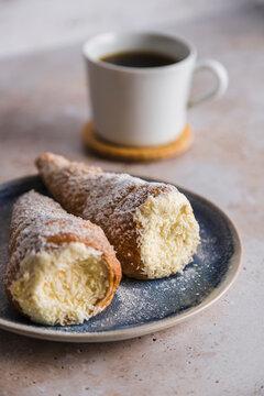 Conic cannoli coated with sugar served with coffee cup