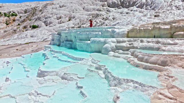 Tourist at Travertines of Pamukkale, Turkey. Tourist walks above turquoise thermal pools surrounded by white limestone terraces in a scenic.