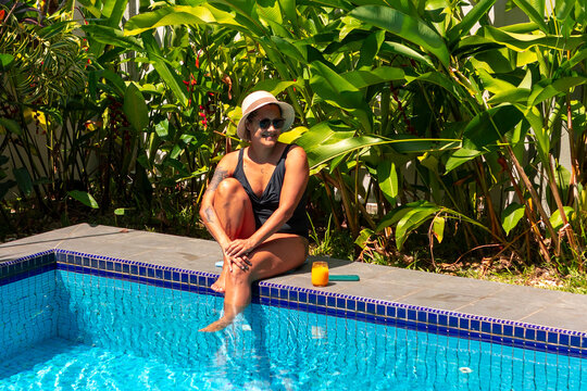 Woman relaxing poolside in tropical garden on summer day