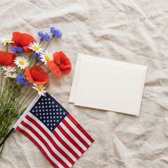 Obraz premium Patriotic flat lay with US flag, spring flowers, and empty greeting card space