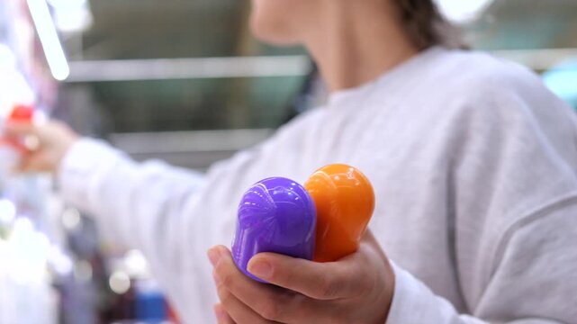 Female customer carefully selecting a deodorant in a supermarket, holding several options in her hands and reading the labels to compare different personal hygiene products before making a purchase