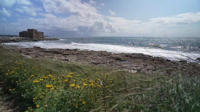 View of Paphos Castle and waves crashing on rocky beach on a sunny day, Paphos, Cyprus