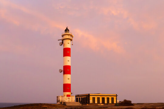 Red and white lighthouse under pastel sunset sky