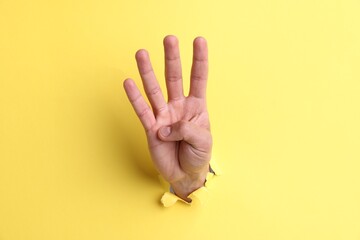 Naklejka premium Man showing number four with fingers through hole in yellow paper, closeup