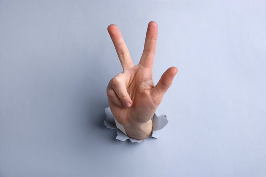 Woman showing number three with fingers through hole in grey paper, closeup