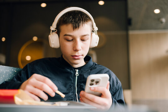 Teenage boy using smartphone with headphone at cafe table