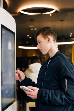 Teenage boy using touchscreen kiosk with smartphone in mall