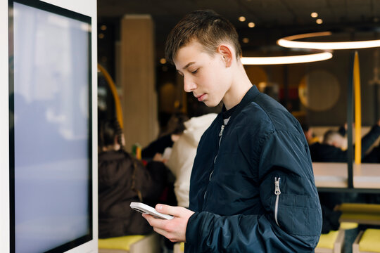 Teenage boy using smartphone near digital display indoors