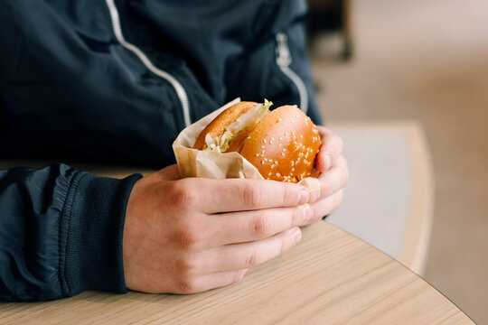 Person holding burger in cafe during quick lunch break