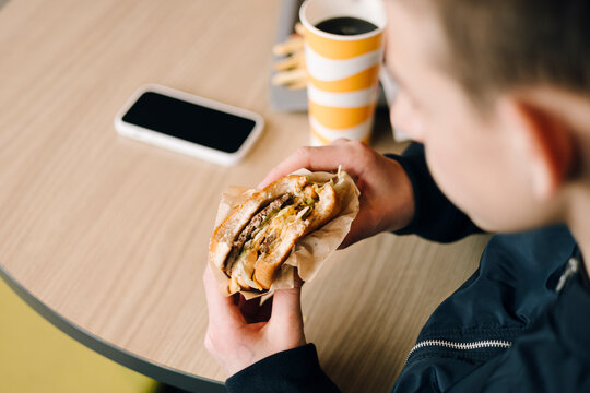 Teenage boy eating burger at table with coffee and phone