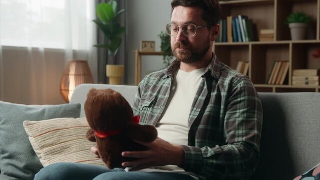 Happy Caucasian man father at home holding cute toy teddy bear preparing gift smiling male guy dad on couch present childish anticipate prepare child children baby custody adoption donation volunteer