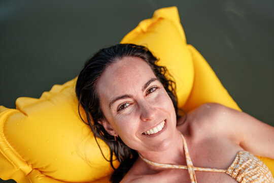 Smiling woman relaxing on yellow float in summer lake