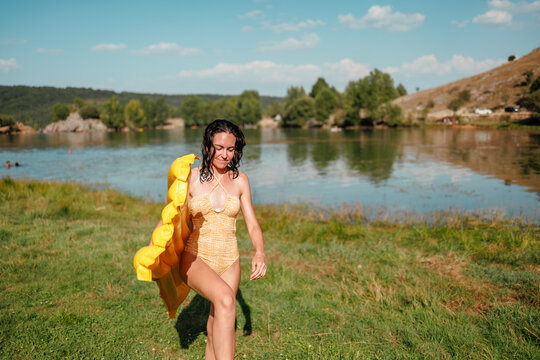 Woman with yellow inflatable walking by lake in summer
