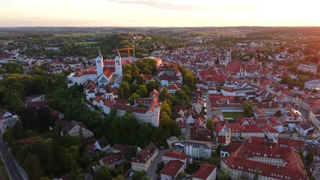 A drone view over Freising, Germany, highlights the Domberg, Freising Cathedral, the Residenzturm, and St. George Church rising above the medieval old town at sunset.