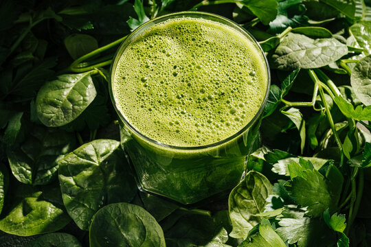 Spinach smoothie in glass on fresh greens background
