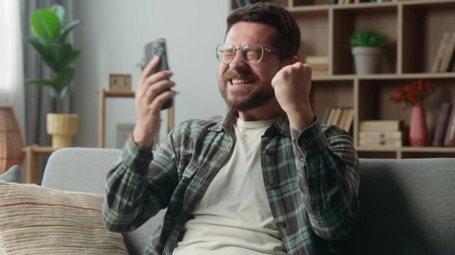 Happy winner Caucasian man at home using mobile phone online victory celebrate cheerful rejoice champion yelling successful guy male gamer user shouting enjoy win video game achieve winning smartphone
