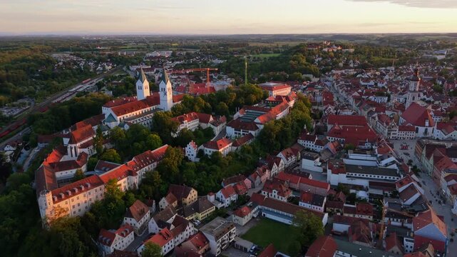 Aerial drone footage captures Freising, Bavaria, Germany, with the Domberg, Freising Cathedral, and St. George Church dominating the old town and city center in soft, glowing sunset light.