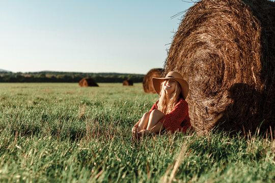 Young woman in field relaxing near hay bale at sunset