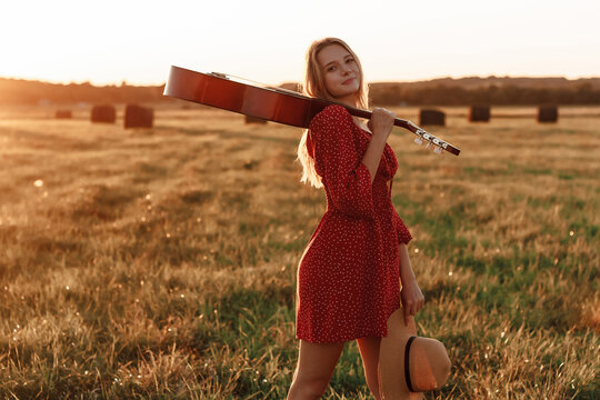 Young blonde in red dress with guitar at sunset