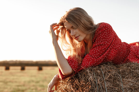 Young woman in red dress on haystack at sunset field