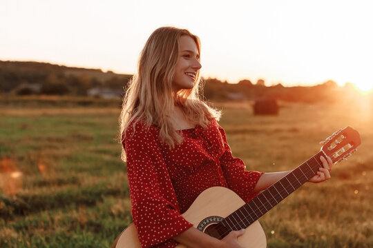 Young woman playing guitar in a sunset field