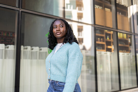 Confident African woman standing by modern city storefront