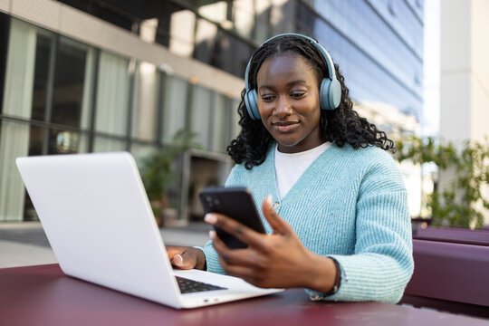 African woman using laptop and smartphone with headphones