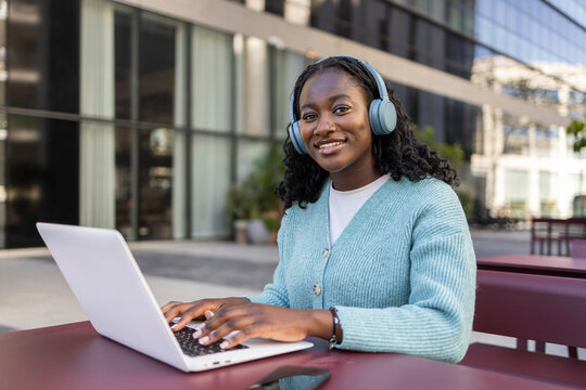 Young African woman with headphones using laptop outdoors