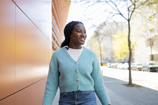 Smiling African woman walking in sunny modern city street