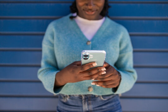 African black woman texting on smartphone by blue wall