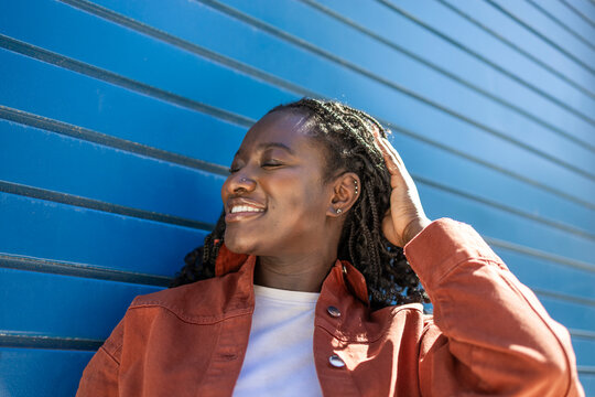Smiling African woman relaxing by blue wall in sunlight