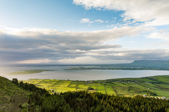 Golden sunset light washes over fields, hills and water near Knocknarea in County Sligo, Ireland. A sweeping aerial view of the Irish landscape at evening.