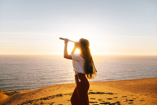Woman gazing through telescope at Concon dunes sunset